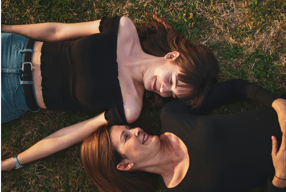 Two women laying on grass facing each other