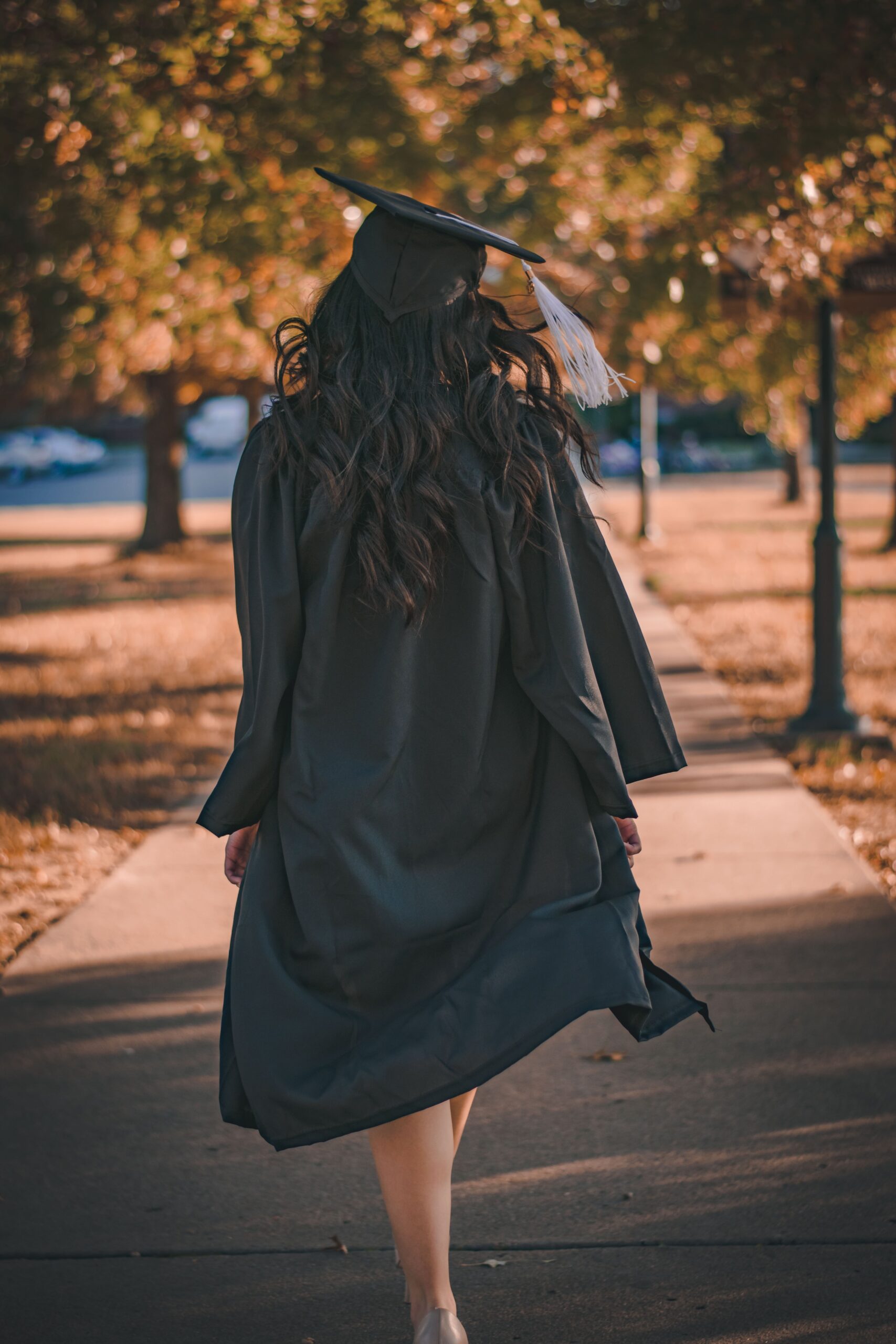 Girl walking away from the camera while wearing a graduation cap and gown.